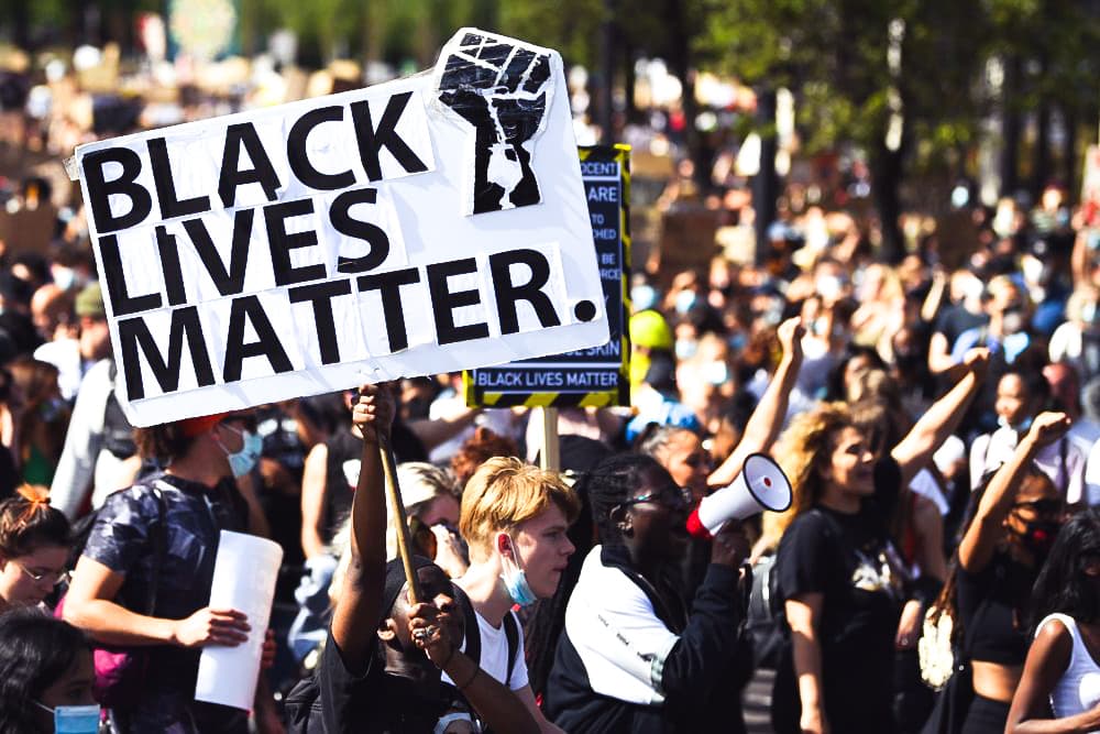 Large crowd of people at a Black Lives Matter rally with fists and posters in the air.